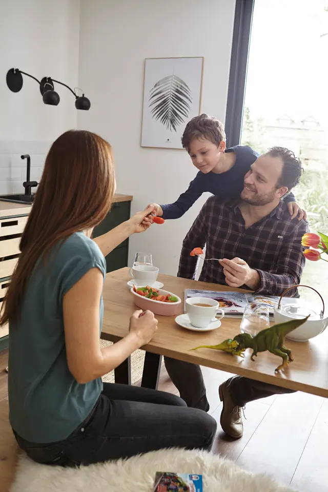 Frau, Mann und Kind sitzen am Tisch in der Küche mit Schalen, Tassen und Tulpen